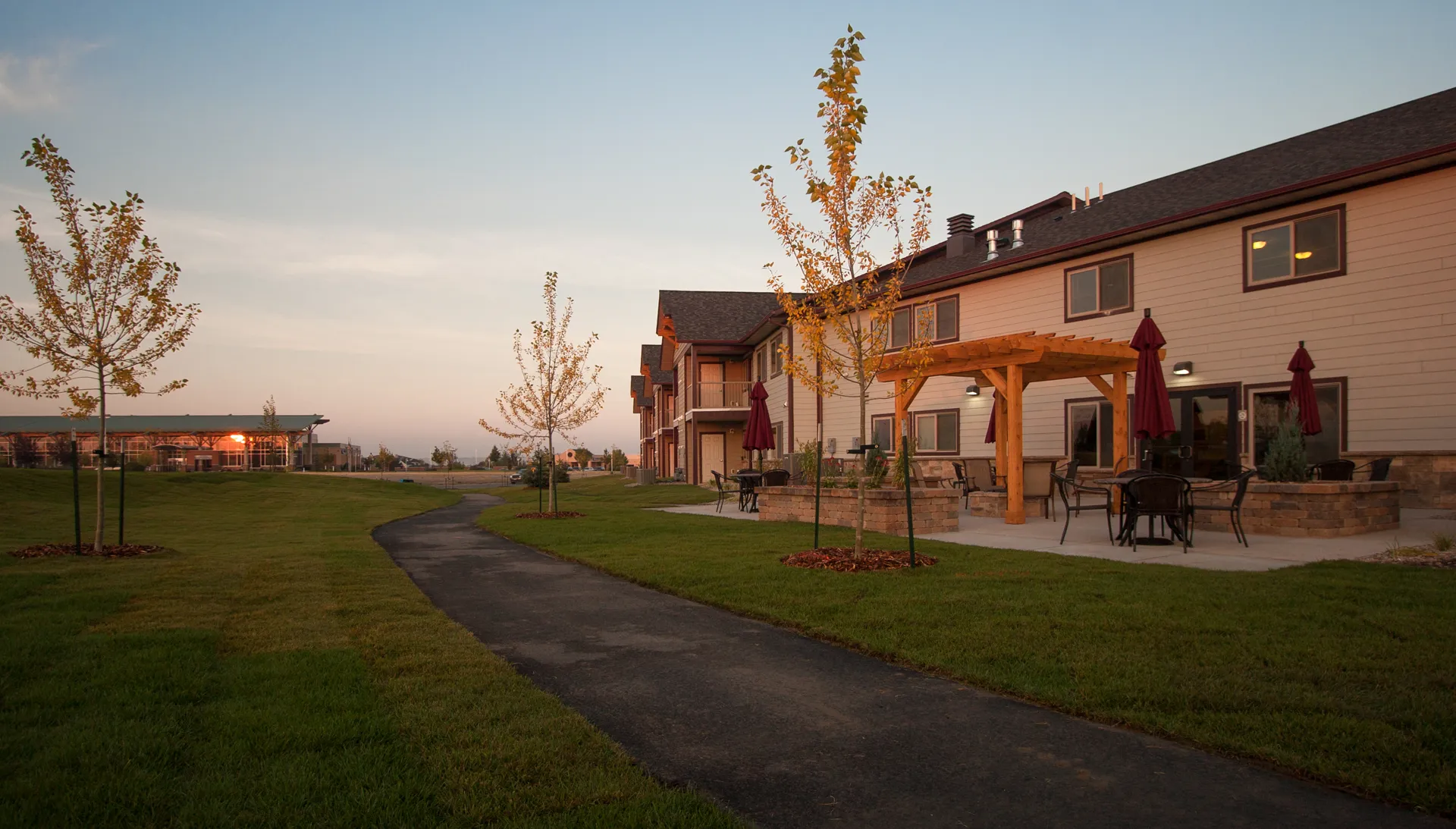 Beautiful suburban homes with well-maintained lawns, trees, and outdoor patio furniture at sunset.