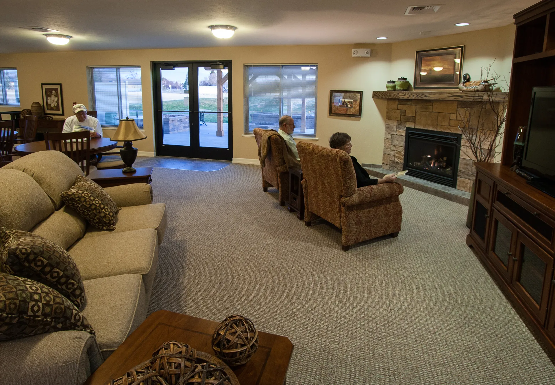 Assisted living lounge with cozy seating, fireplace, and large windows.