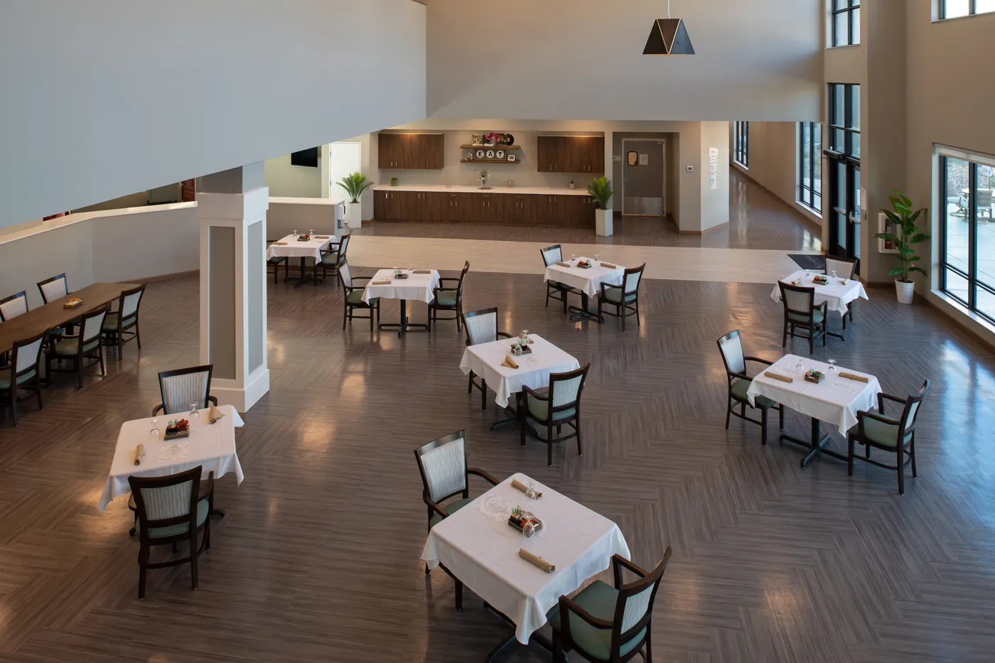Modern restaurant interior with dining tables, chairs, and large windows for natural light.