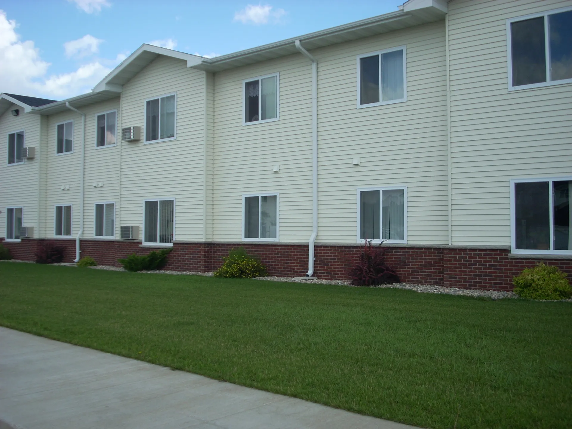 Modern residential apartment building with white siding and brick foundation.