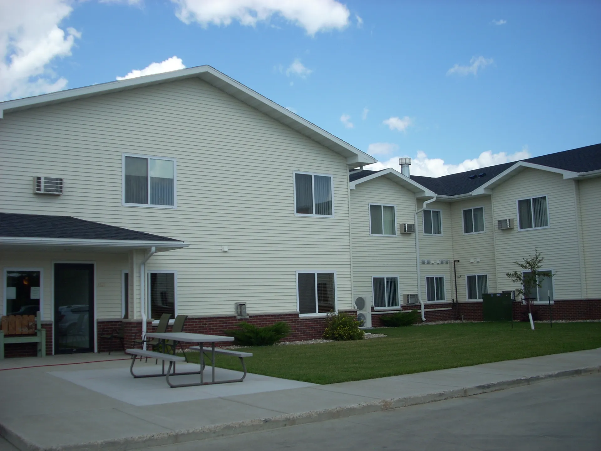 Apartment complex with white siding, multiple windows, and outdoor seating area.