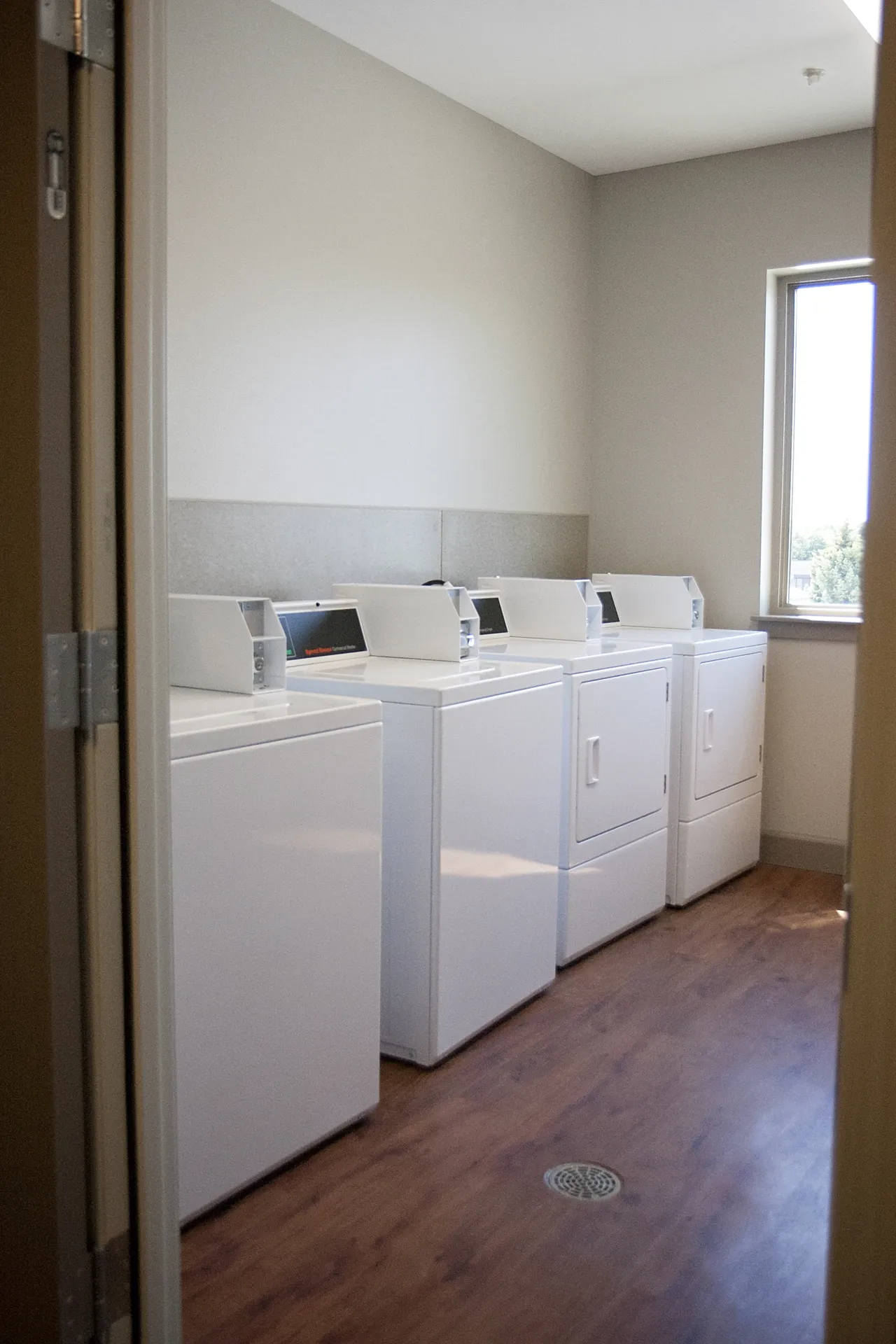 Laundry room with white washing machines and dryer, natural light from window.