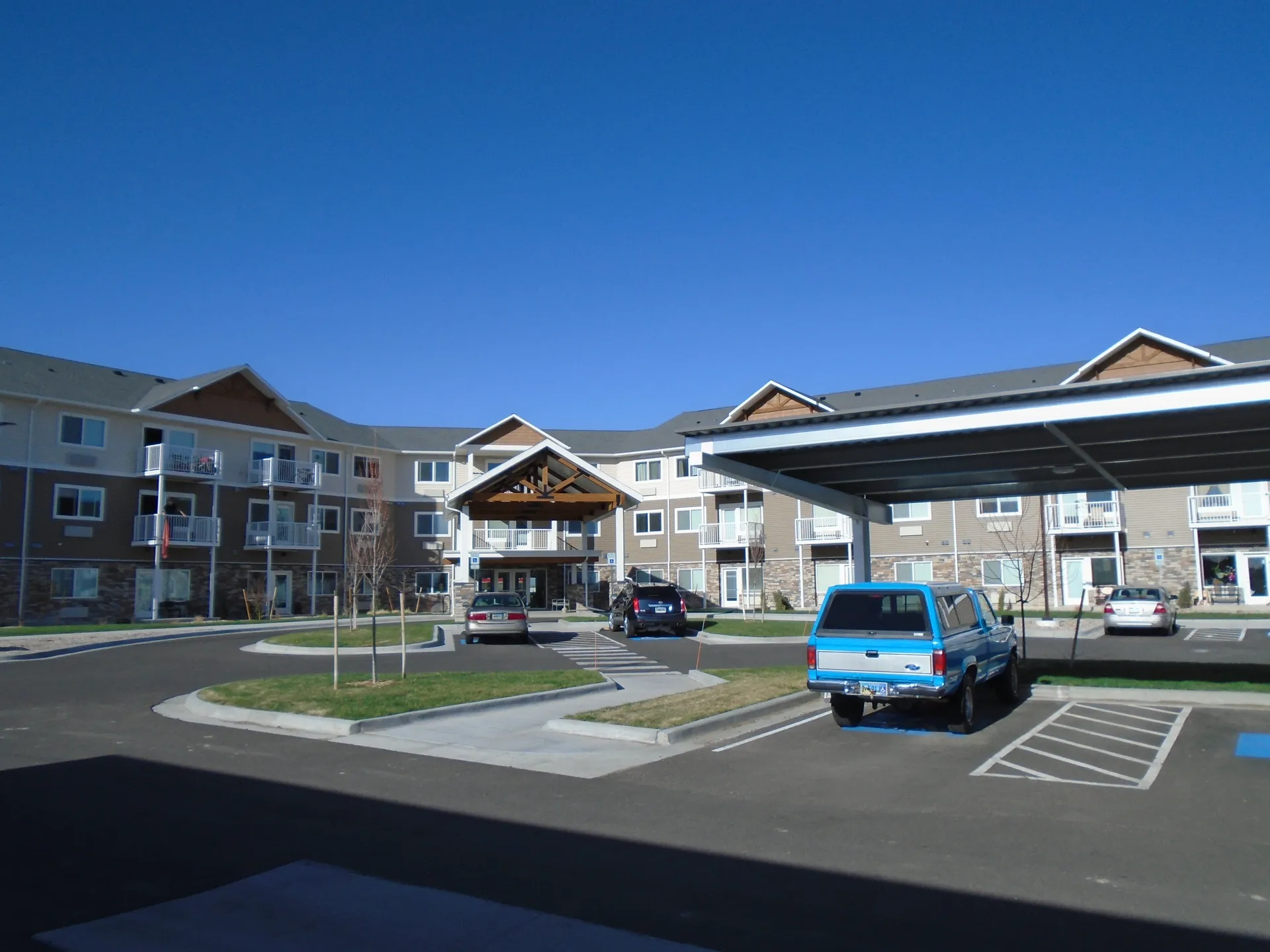 Apartment complex with parking lot and solar panels under clear blue sky.