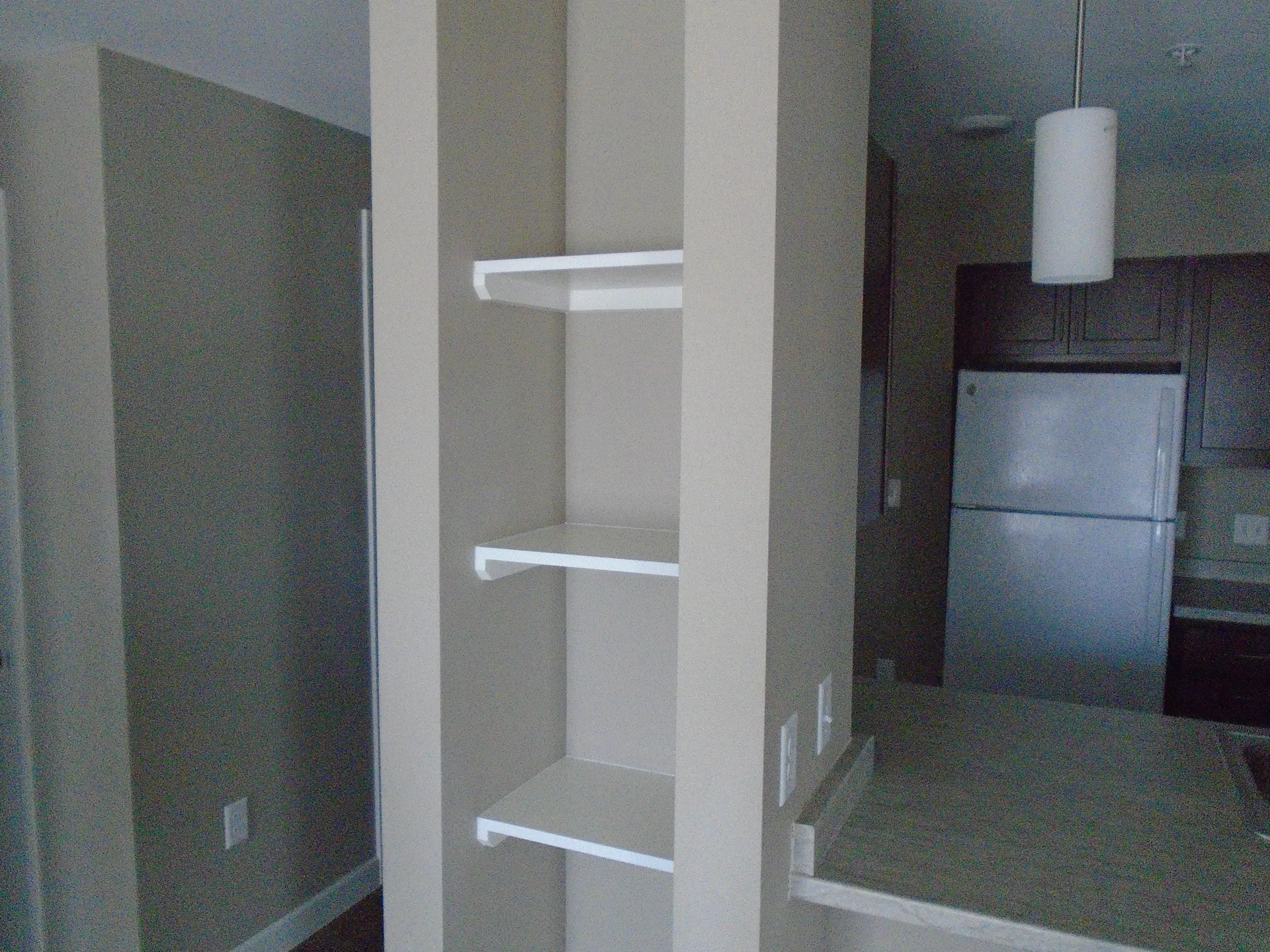 Built-in shelves in a contemporary kitchen with stainless steel refrigerator and modern decor.