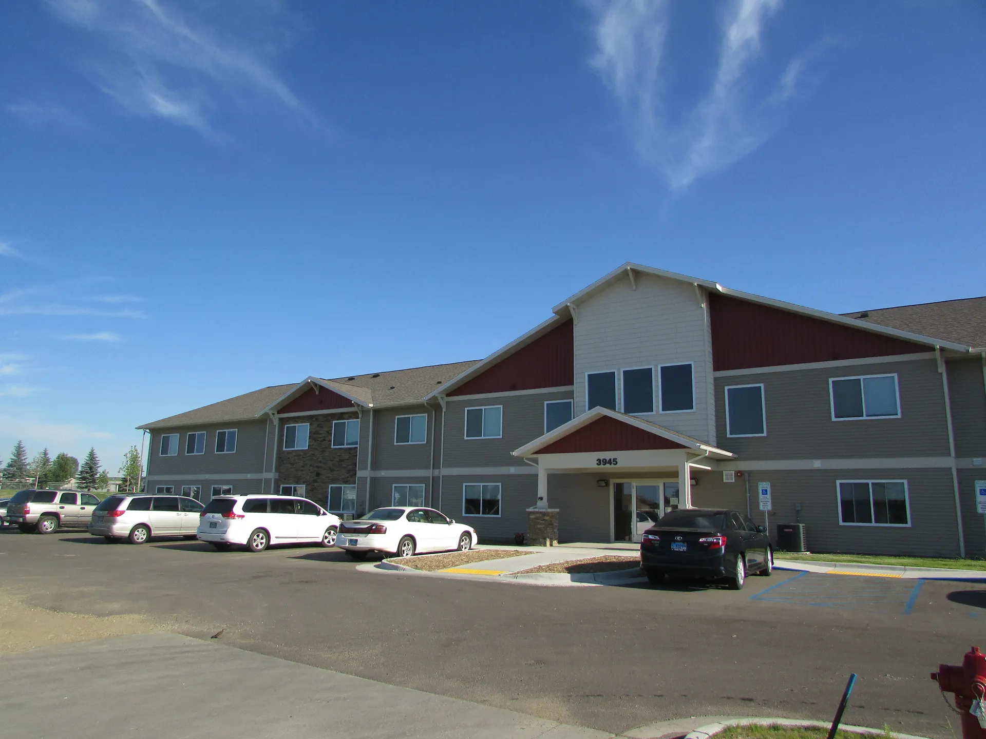 Modern multi-family residential building with parking lot in front, featuring multiple units and con.