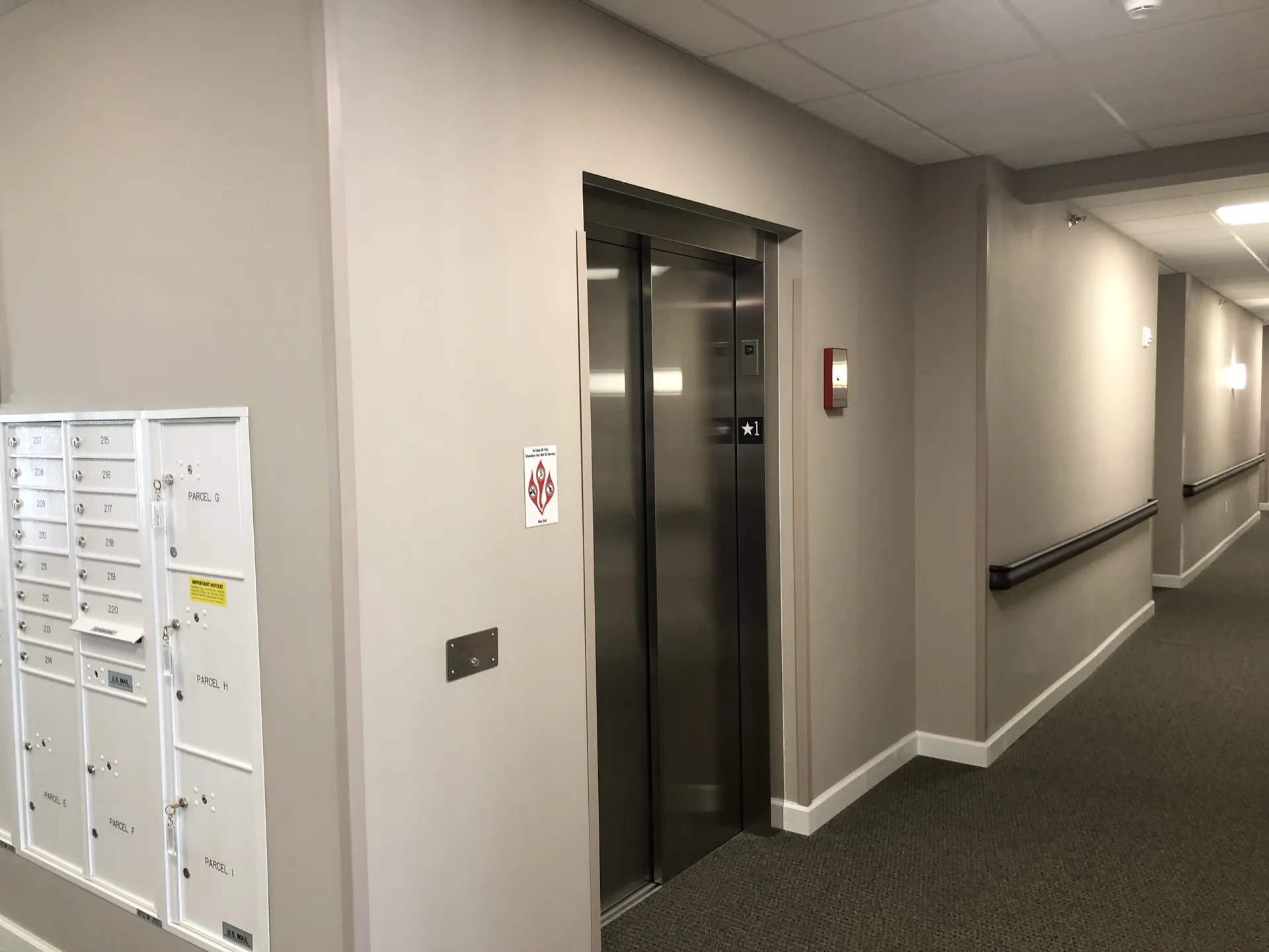 Elevator in a professional office corridor with clean, neutral-colored walls and safety features.