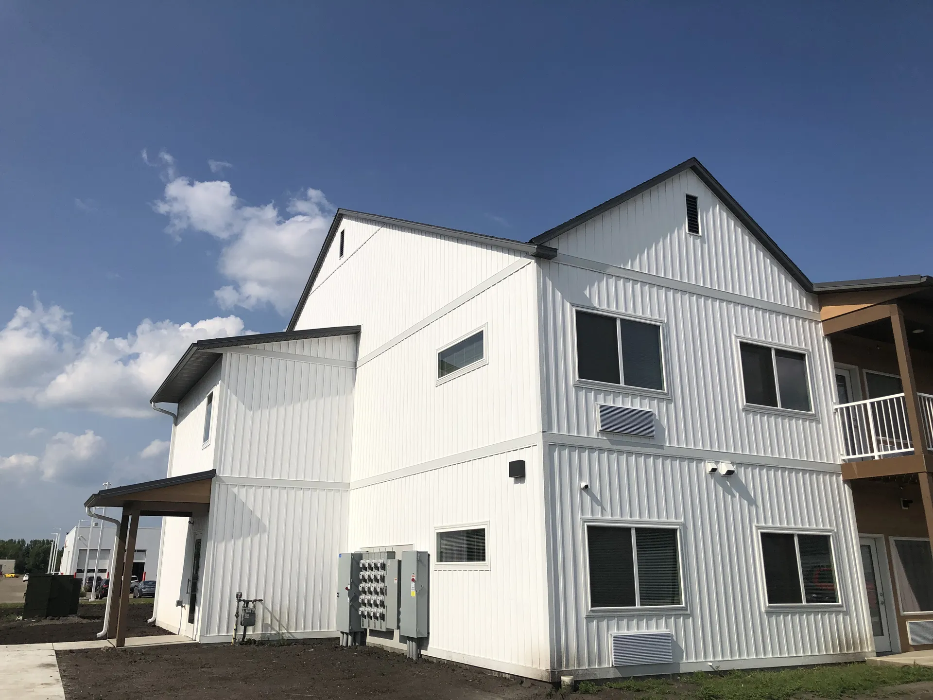 Modern white multi-family residential building with metal siding and multiple windows.
