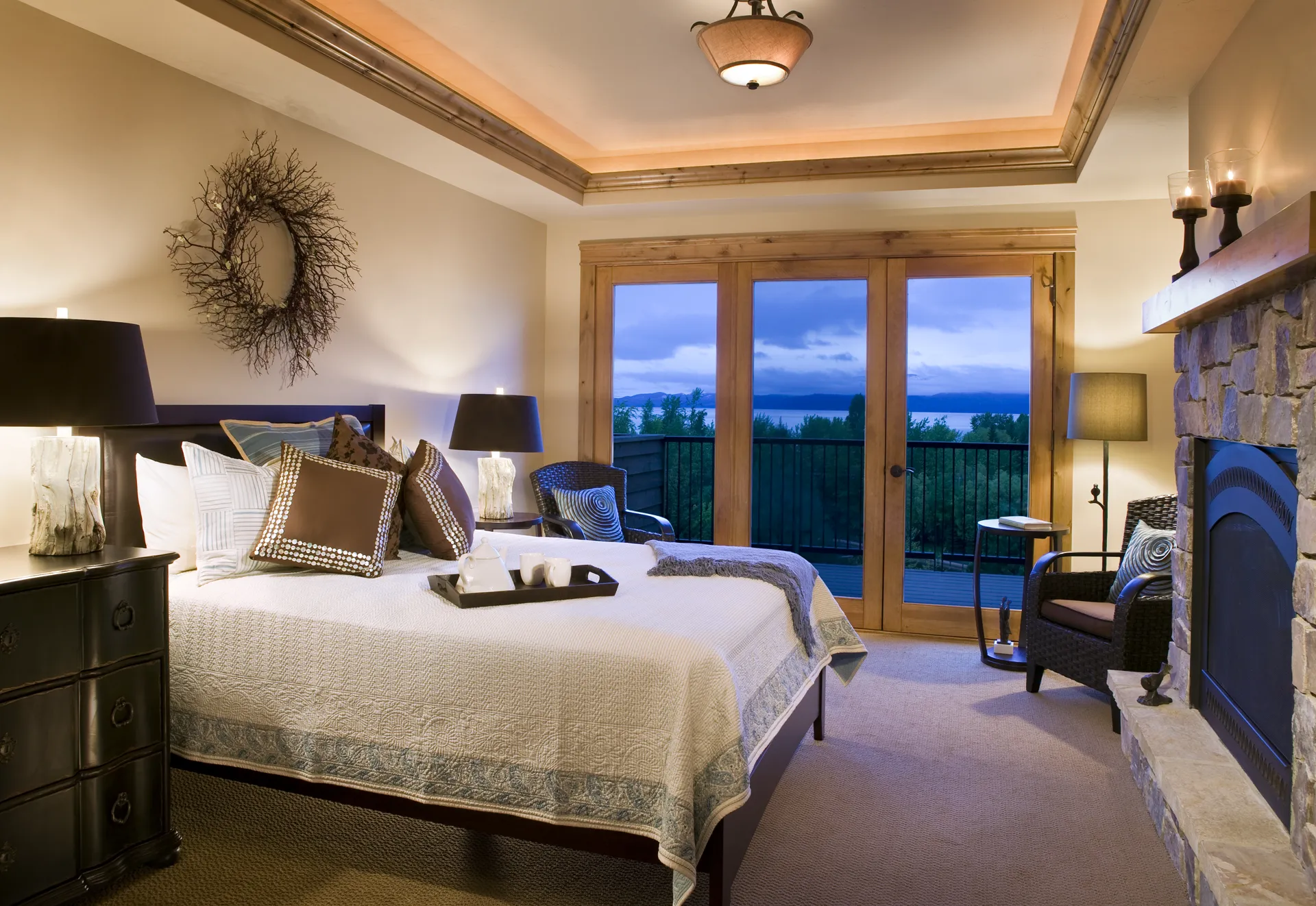 Comfortable bedroom featuring a stone fireplace, large windows with a mountain view, and elegant dec.