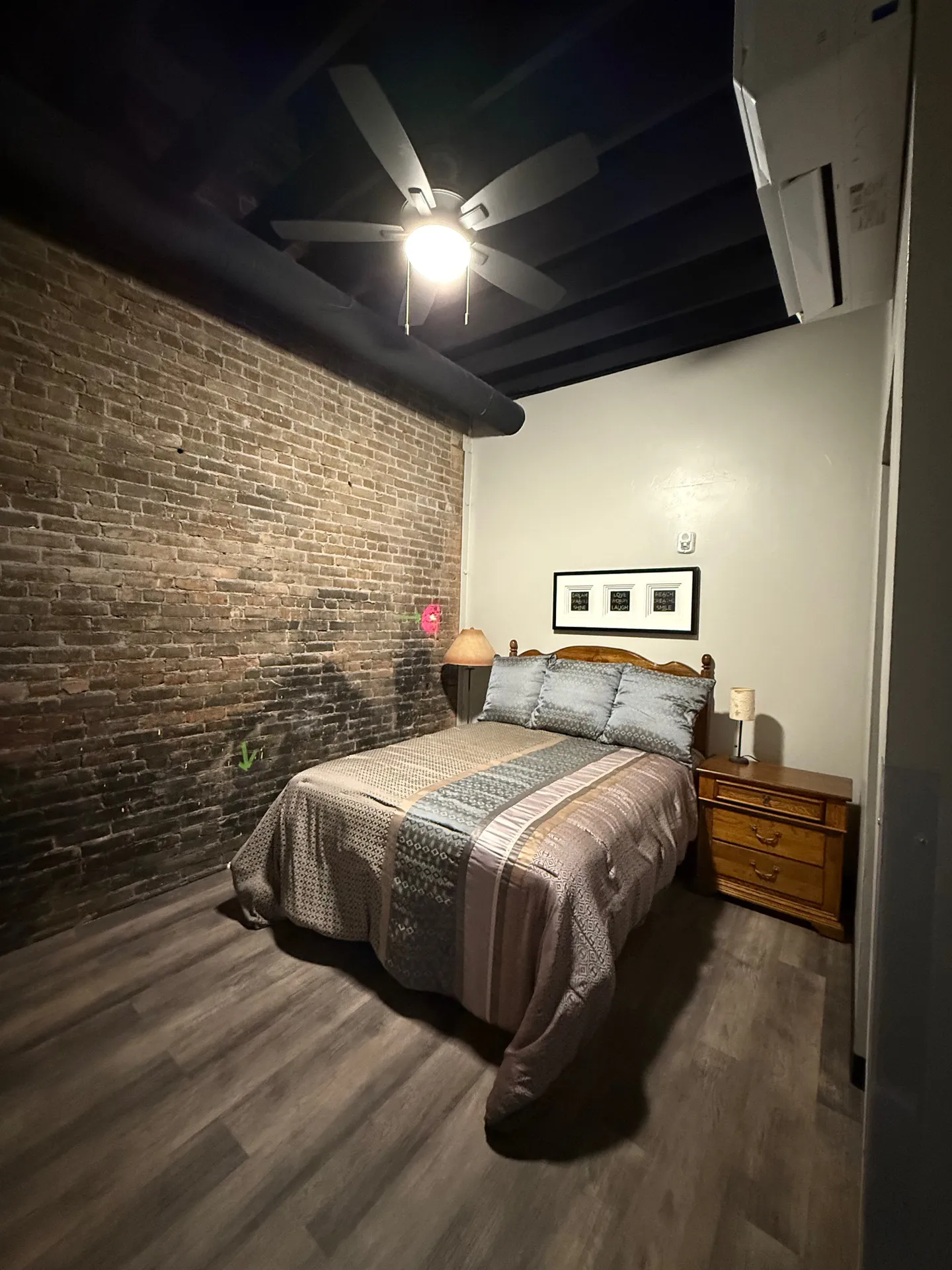 Cozy bedroom featuring a brick accent wall, ceiling fan, and stylish bedding for a comfortable retre.