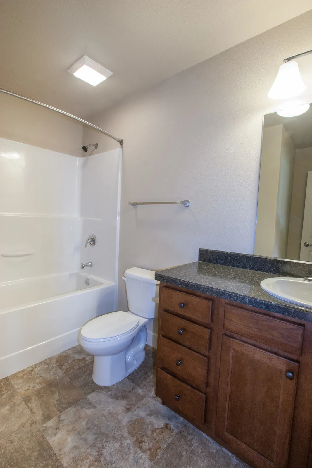 Bathroom with bathtub, toilet, and wooden vanity featuring granite countertop.