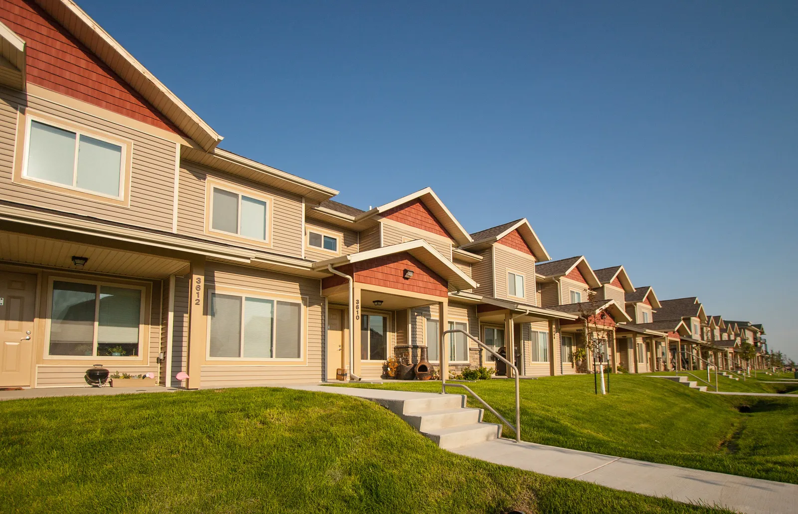 Townhouse residential buildings with landscaped lawns and a bright, sunny sky.