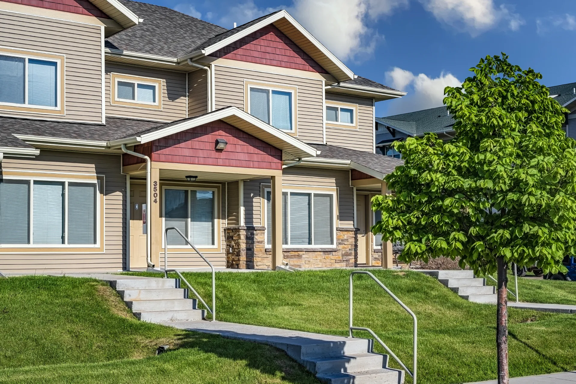 Beautiful suburban home with well-maintained lawn, trees, and accessible stairs.