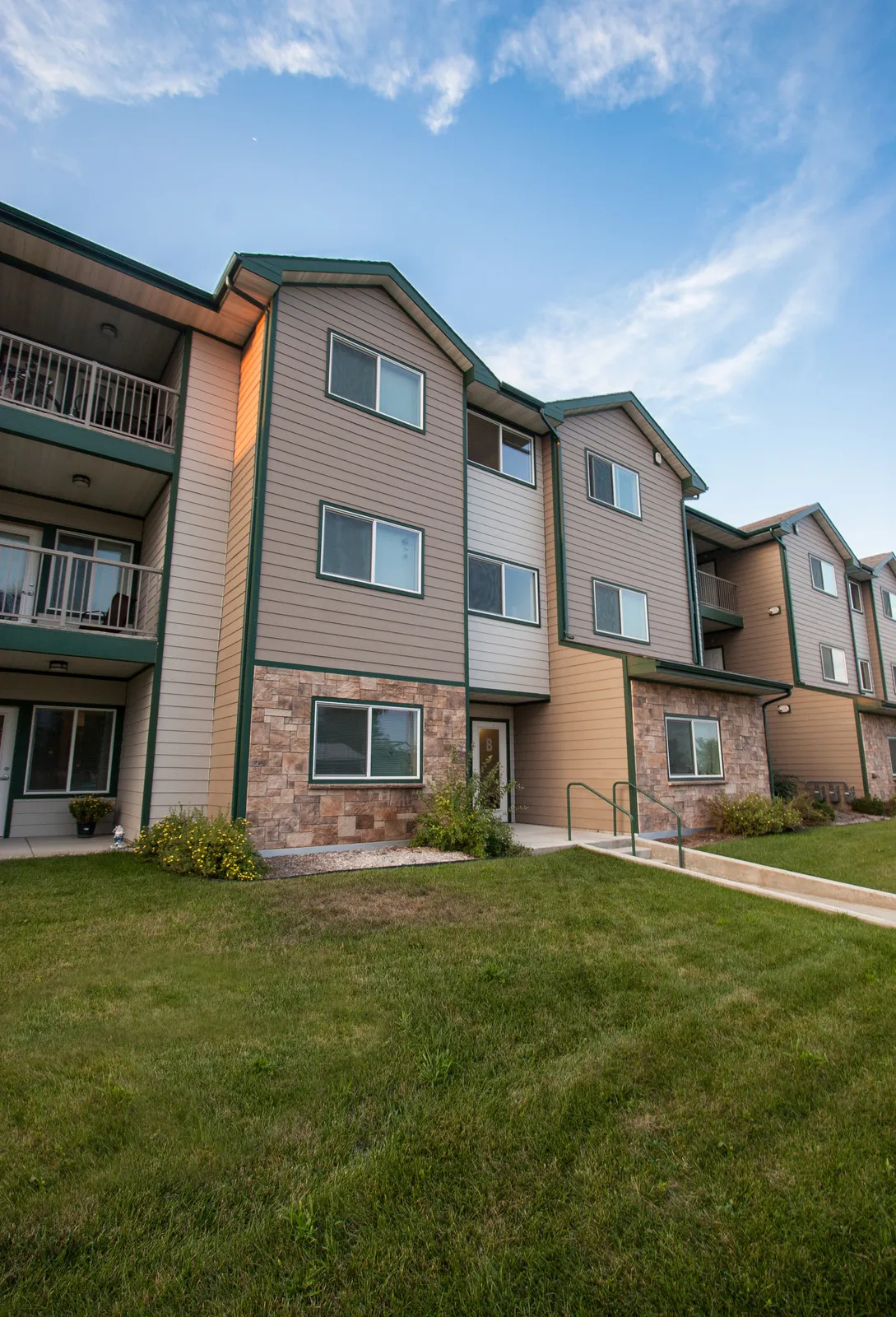 Apartment building with beige siding, brick accents, and multiple windows.