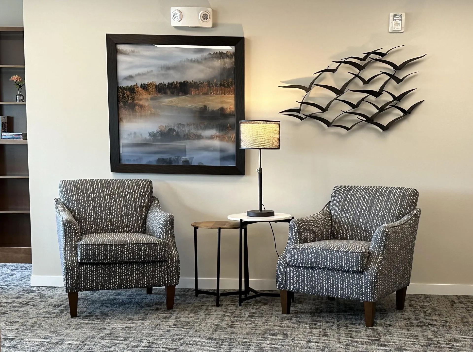 Comfortable waiting room with two upholstered chairs, a side table, and decorative wall art.
