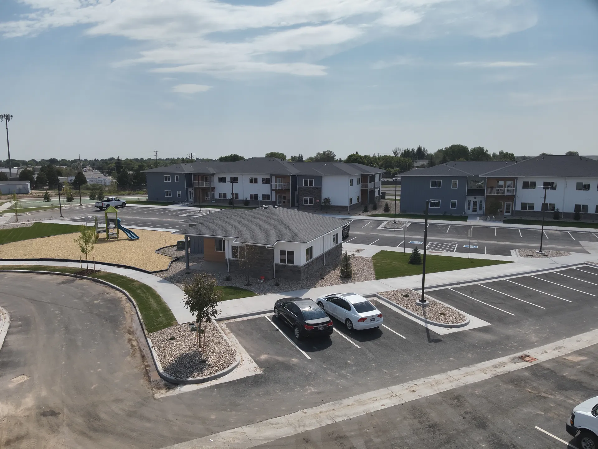 Apartment complex with parking area, landscaped lawns, and modern residential buildings.