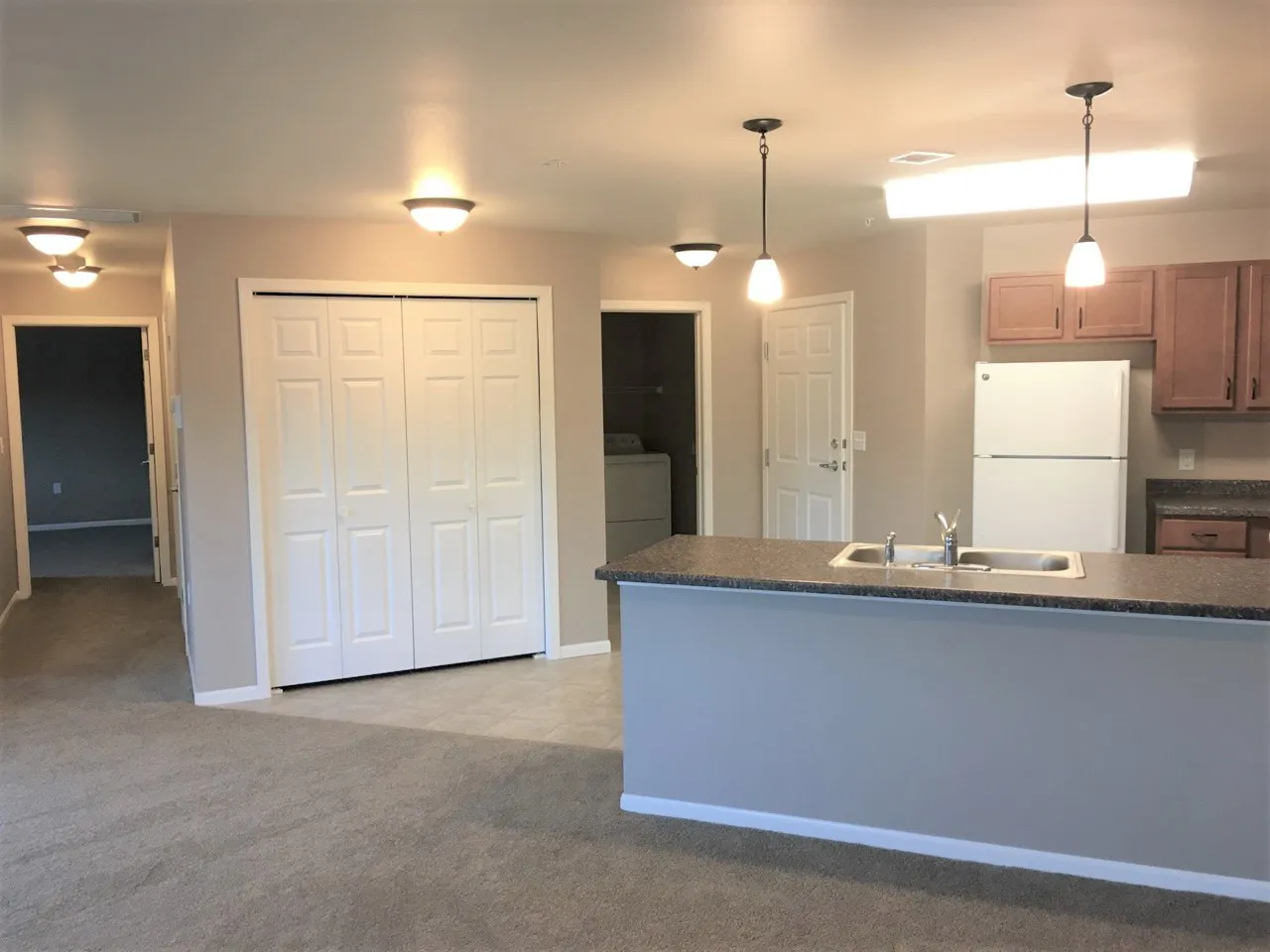 Modern kitchen with island and pendant lighting, open to living area, featuring wooden cabinets and.