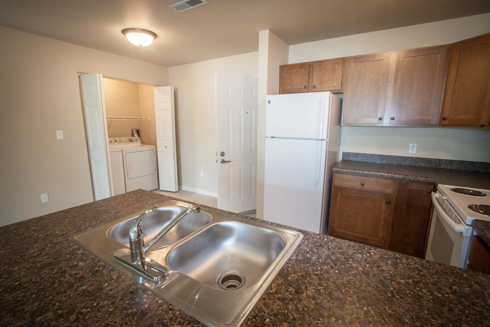 Kitchen with wooden cabinets, white refrigerator, and stainless steel sink.