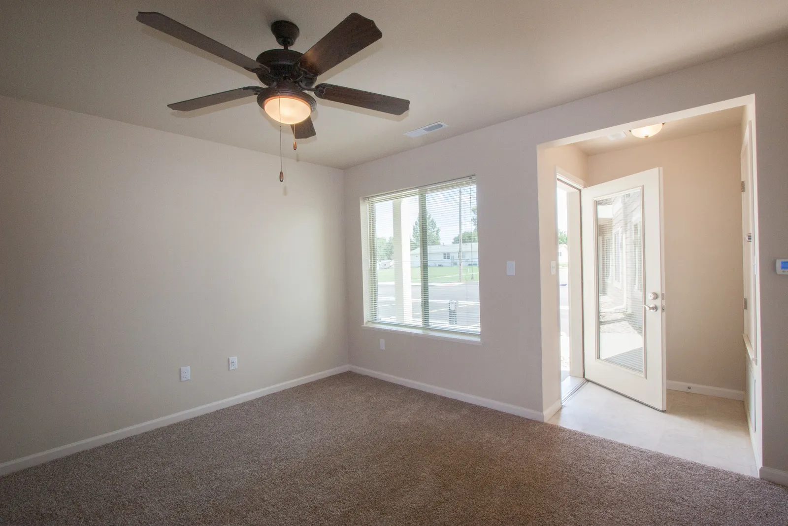 Ceiling fan installed in a bright, empty living room with large windows and an open door leading out.
