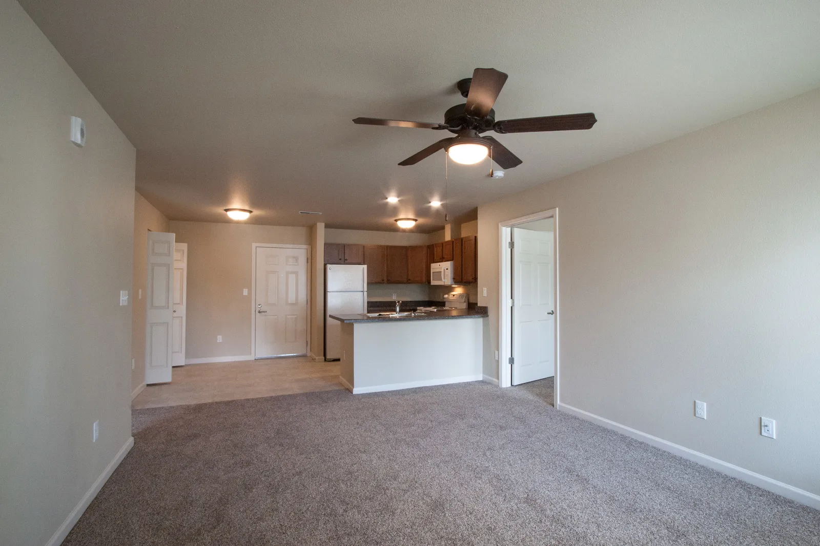 Renovated living room featuring a modern open kitchen, ceiling fan, and neutral decor, perfect for c.