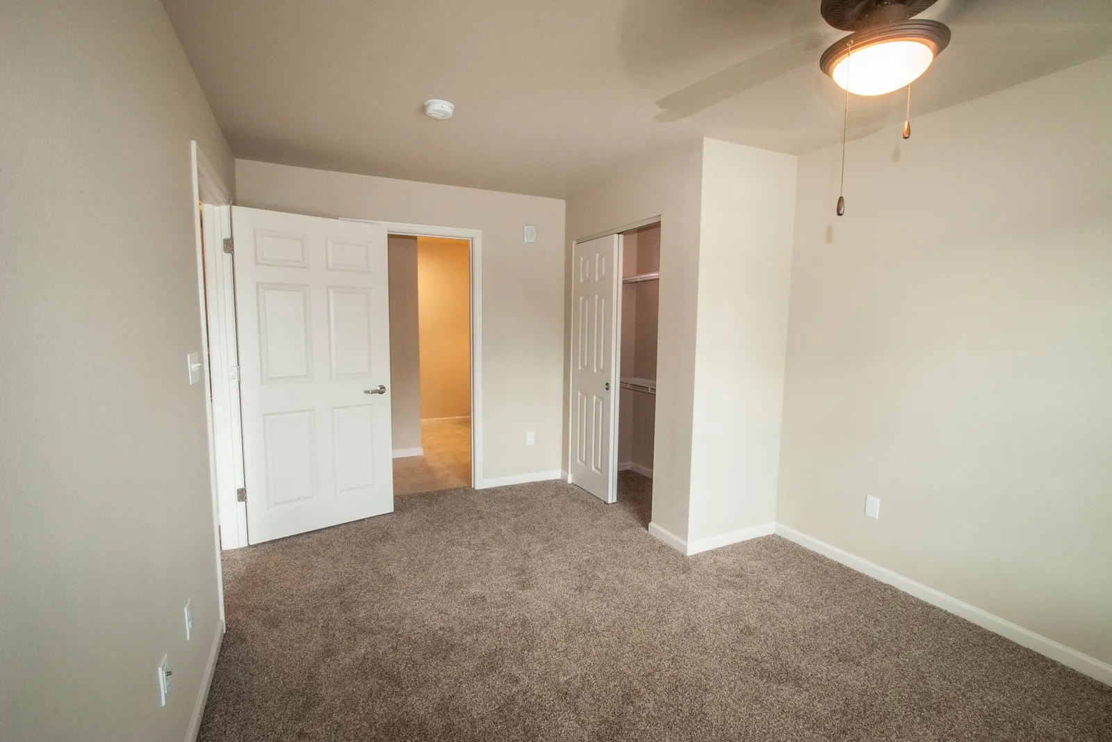 Interior room with beige walls, plush carpet, and ceiling fan, showcasing a clean, renovated living.